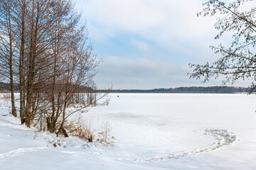 Winter landscape with frozen lake and deciduous trees on a sunny day