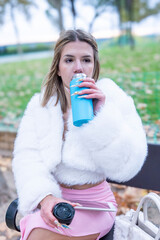 Influencer drinking from reusable bottle in park while holding tablet and portable speaker