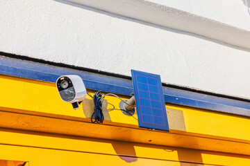 Outdoor security camera mounted on yellow wall with solar panel, capturing sunlight for eco-friendly surveillance. Sweden. © Alex