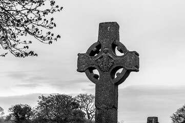 A black and white photo of a stone cross with a tree in the background