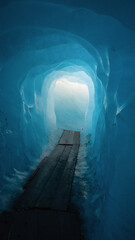 Obraz premium Inside Rhône Glacier. Light at the end of the blue ice grotto. Wooden walkway in tunnel inside a glacier.