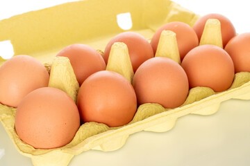 A dozen chicken eggs in a paper box, close-up, isolated on a white background.