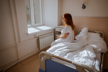 An unhappy pregnant woman sits on a couch in a hospital room.