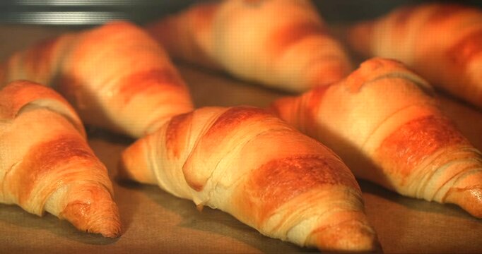 Delicious croissants are baking in the oven, transforming into golden products while filling the kitchen with a warm aroma just before breakfast time.