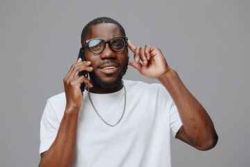 African male model in casual attire, using a smartphone, expressing joy and excitement against a neutral gray background Stylish glasses enhance the modern look