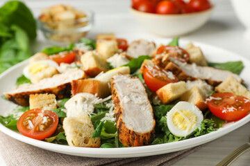 Tasty Caesar salad with chicken and tomatoes on white wooden table, closeup