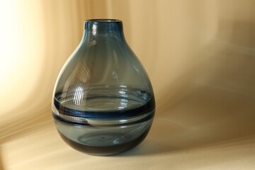 Empty glass vase on beige background, space for text