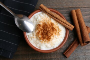Delicious rice pudding with cinnamon sticks on wooden table, top view