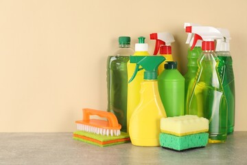 Different cleaning products and supplies on grey table against beige background, space for text