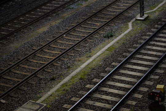 Parallel train tracks stretch across a gravel-covered area with patches of grass growing between them