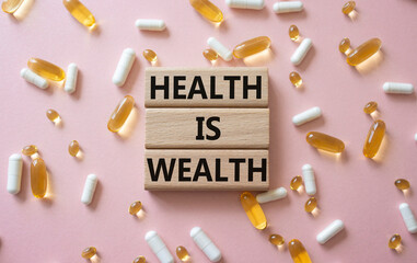 Health is Wealth symbol. Concept word Health is Wealth on wooden blocks. Beautiful pink background with pills. Medicine and Health is Wealth concept. Copy space