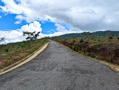An infinite road leading to a mountain range, with a beautiful blue sky and clouds, captured in Palahirigala, Sri Lanka.
