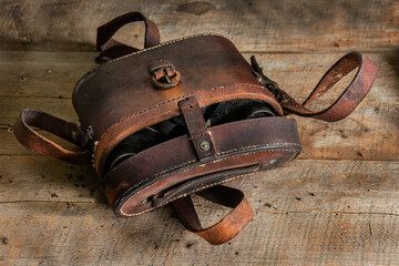 old weathered leather binocular case on wooden bench