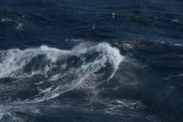 powerful ocean waves crash against each other, creating dramatic scene of turbulent water and frothy white caps. deep blue hues of sea evoke sense of awe and respect for nature force