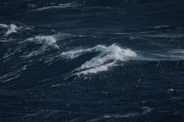 Dark ocean waves create dramatic scene with foamy crests and turbulent waters, evoking sense of power and mystery