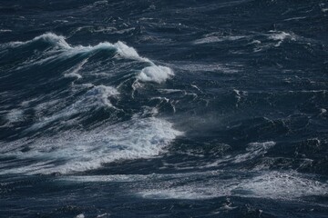 Rough ocean waves crashing against each other create dramatic seascape. deep blue water contrasts with white foam, evoking sense of power and movement