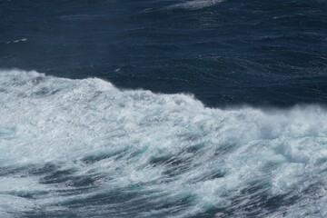 Waves crashing on dark ocean surface create dynamic and powerful scene. frothy white foam contrasts beautifully with deep blue water, evoking sense of nature raw energy