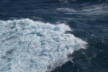 image captures dynamic ocean scene with waves crashing and frothy white water against deep blue sea, evoking sense of power and tranquility