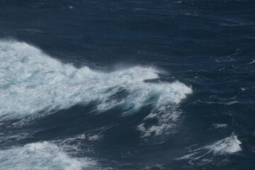 Waves crashing on dark ocean surface create dynamic and powerful scene. contrast of white foam against deep blue water evokes sense of nature raw energy and beauty