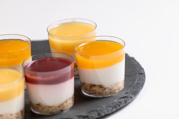 Dessert Shots, Cheesecake in glasses with raspberry and mango topping, desserts on a black stand and white background, in various pannacotta,