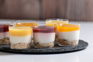 dessert with cream, Dessert Shots, Cheesecake in glasses with raspberry and mango topping, desserts on a black stand and white background, in various pannacotta,