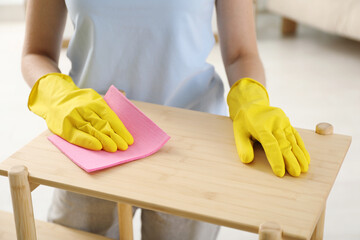 Young woman cleaning wooden shelf with rag at home, closeup