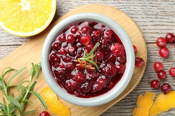 Tasty cranberry sauce in bowl, berries, orange and rosemary on wooden table, flat lay