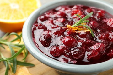Tasty cranberry sauce in bowl, orange zest and rosemary on table, closeup