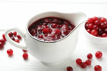Tasty cranberry sauce in gravy boat and berries on white wooden table, closeup