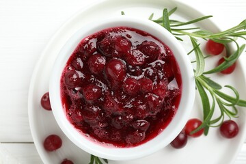Tasty cranberry sauce in bowl, berries and rosemary on white table, top view