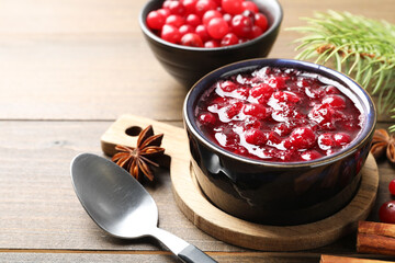 Tasty cranberry sauce in bowl, berries, spices and fir tree branch on wooden table, closeup