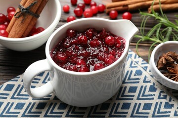 Tasty cranberry sauce in gravy boat and spices on table, closeup