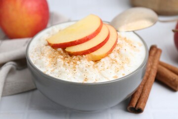 Delicious rice pudding with apples and cinnamon on white tiled table, closeup