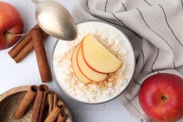 Delicious rice pudding with apples and cinnamon on white tiled table, flat lay