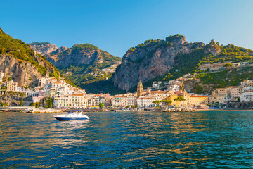 Fototapeta premium The photo captures a sunny view of Amalfi, showcasing the town's colorful buildings, steep cliffs, and vibrant coastline under a clear blue sky on a bright day.