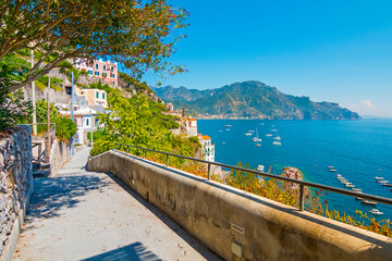 The photo captures a sunny view of Amalfi, showcasing the town's colorful buildings, steep cliffs,...