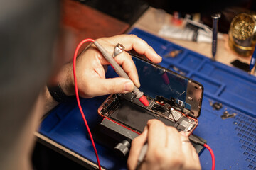 Technician performing smartphone battery repair on a device at a workshop in the evening