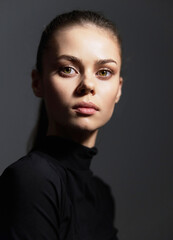 Thoughtful young woman in black turtleneck, gazing at the camera with an intense expression....