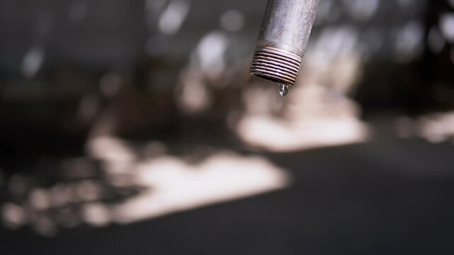 Close-up of water drops falling from a leaking pipe. This symbolizes water scarcity and plumbing issues.