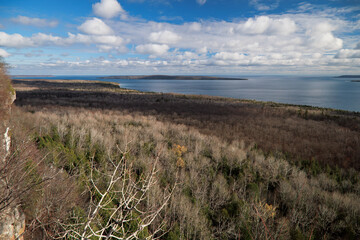 The Georgian Bay coastline wilderness at Colpoy’s Bay, of trees, forest, blue water, blue sky, puffy white clouds, islands, and the cliffs of the Niagara Escarpment. 