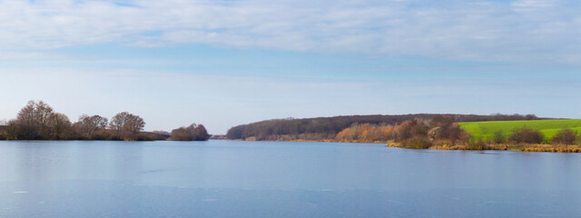 spring landscape with a wide calm river near the forest and a clear sky with white clouds