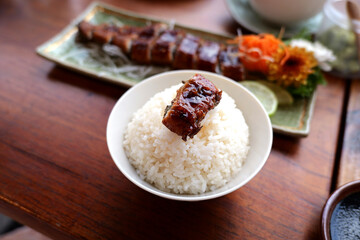 Delicious rice bowl topped with savory grilled meat, garnished with colorful vegetables.