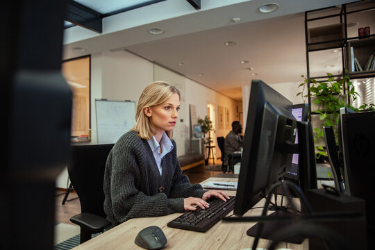 Focused woman working at dual monitors in modern office setting