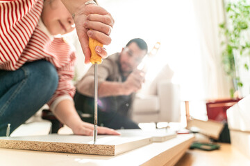 Obraz premium Happy Couple Assembles Furniture as a Team, Girl Reads Instructions and Boy Tightens Screw with a Drill. Moving into New Apartment, Couple Assemble Shelf.