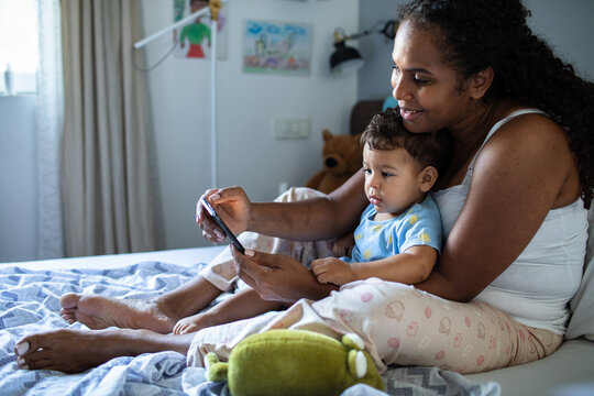 Smiling mother showing smartphone to toddler son at home