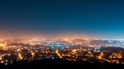 Naklejka premium Beautiful panoramic night cityscape with glowing orange lights across urban landscape. Aerial view of illuminated city at dusk with deep blue sky. Urban photography for tourism, real estate with copy 