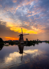 A windmill stands tall against a vibrant sunset, reflection the beauty of the sky in the canal