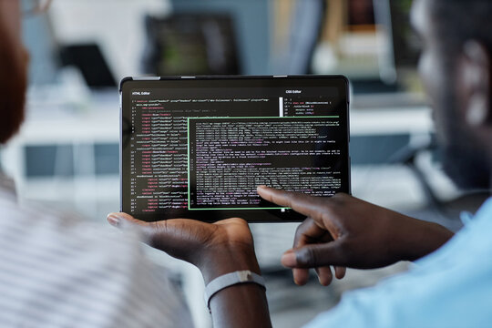 Close-up of two individuals reviewing code displayed on a tablet device with a blurred office background showcasing a collaborative tech workplace moment