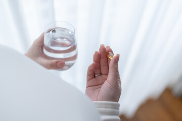 Pregnant woman holding a glass of water, taking vitamins and minerals during pregnancy. Pregnancy, health, pharmaceuticals. Close up photo