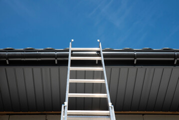 Aluminium ladder leans against the roof of the house © Sergey